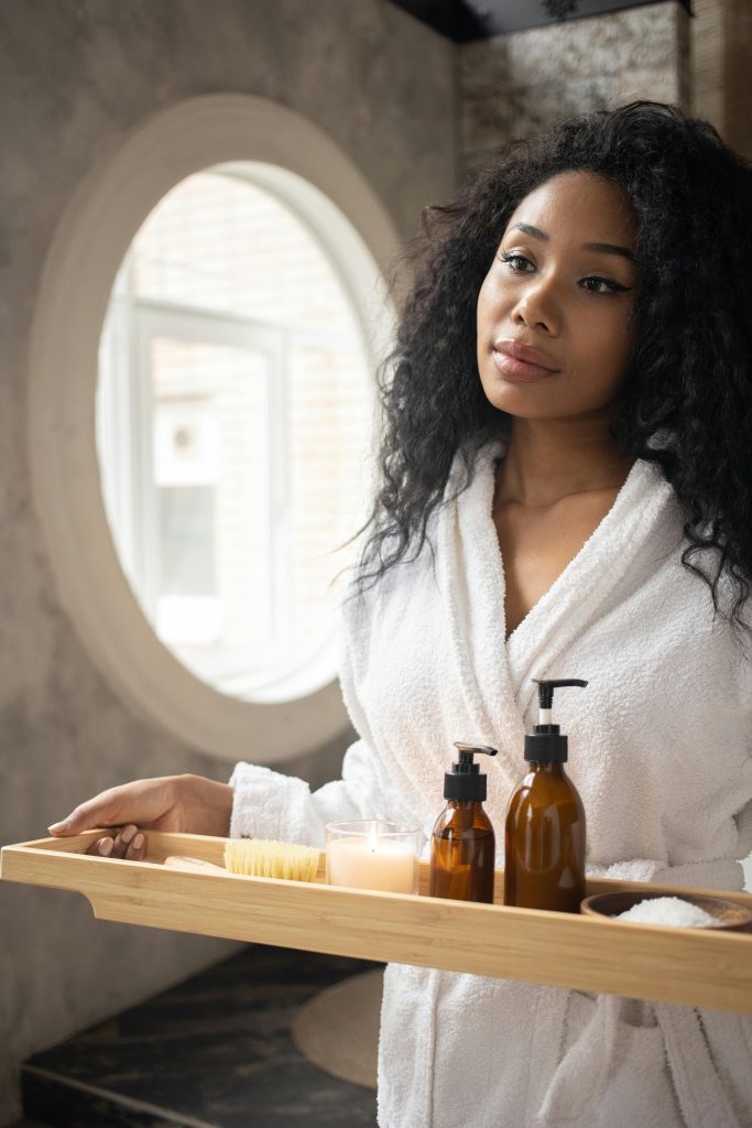 a person in a bathrobe holding a tray of soap and a candle